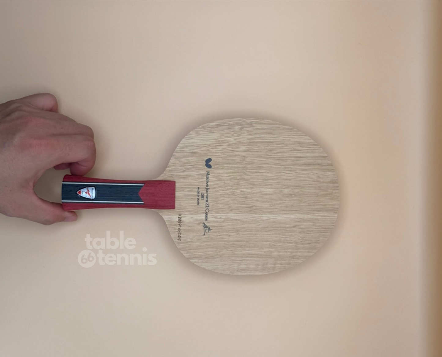 Table tennis paddle held by a hand on a beige background