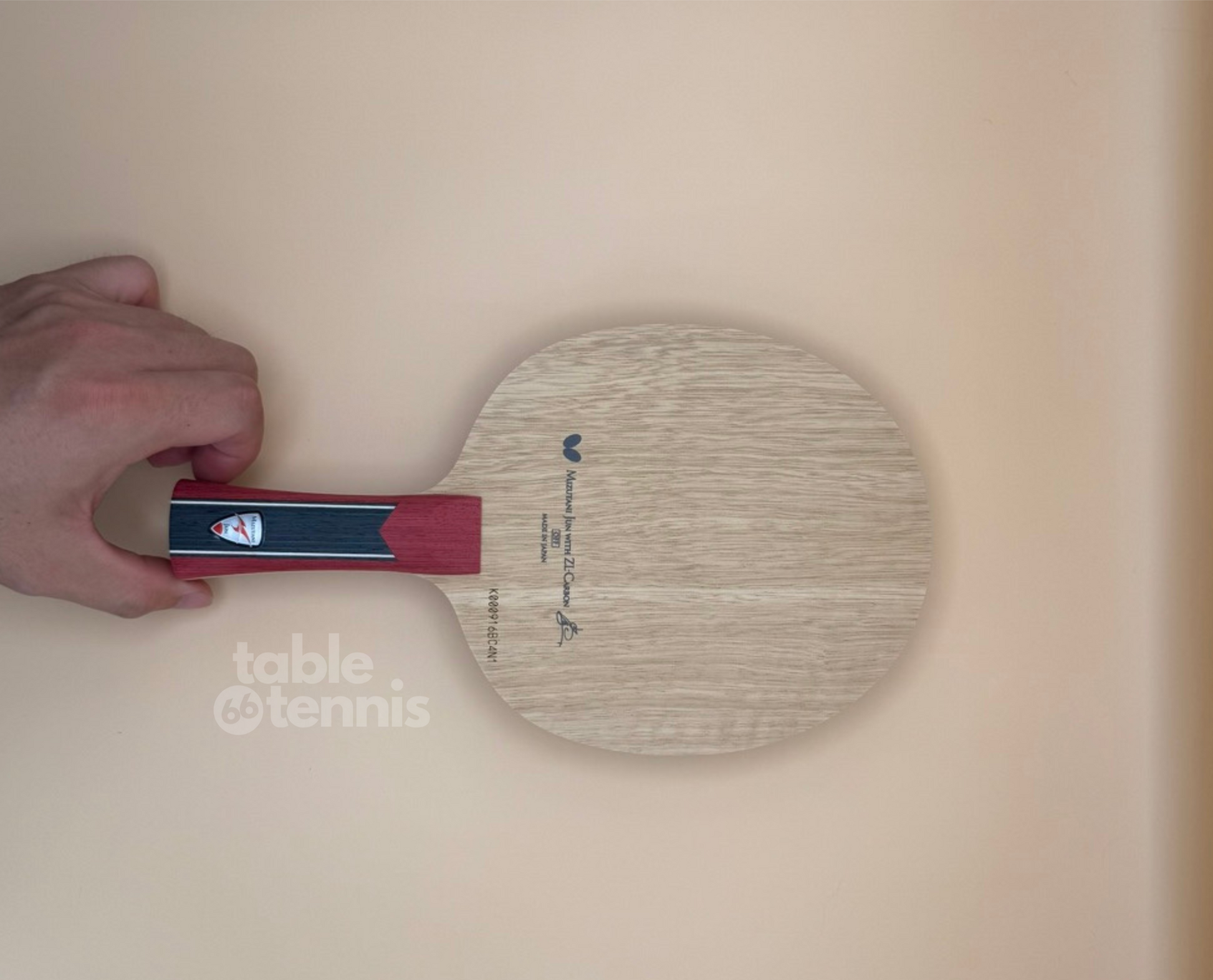 Table tennis paddle held by a hand on a beige background